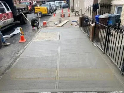 Crew member finishing a newly poured residential sidewalk with the work truck parked nearby