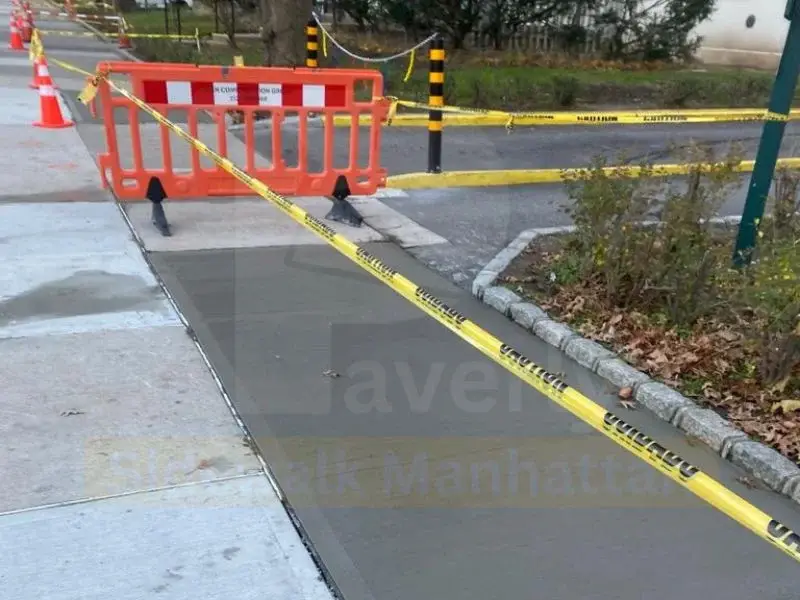 New concrete sidewalk poured flush against a granite block curb behind a safety barricade