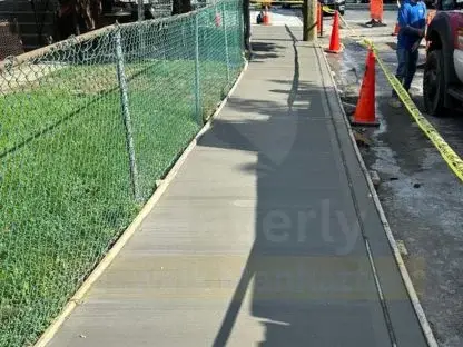 Long run of newly finished concrete sidewalk with smooth, even joints along a fenced lot
