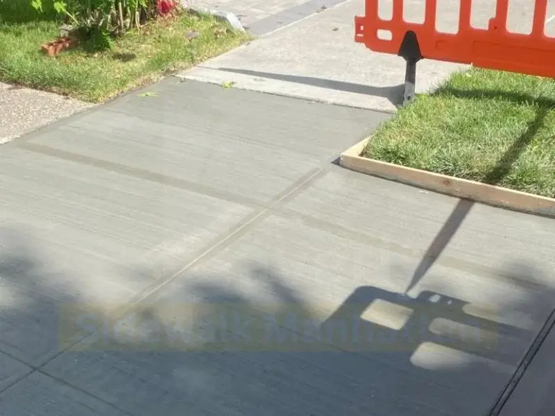 Freshly finished concrete sidewalk slab with wood forms still in place along a lawn