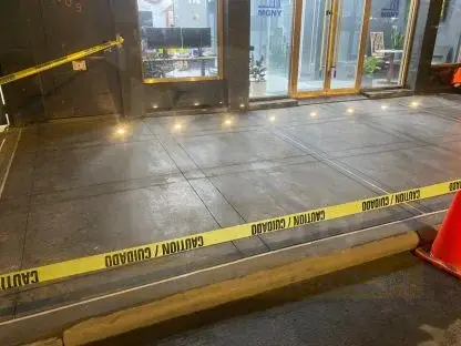 Newly replaced concrete sidewalk in front of a glass storefront, taped off in the evening